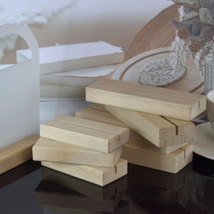 Könnte beinhalten: Ein Satz aus sechs natürlichen Holz-Schildhaltern. Die Halter sind übereinander gestapelt und aus unbehandeltem Holz gefertigt. Die Halter sind so konzipiert, dass sie kleine Schilder oder Karten halten.