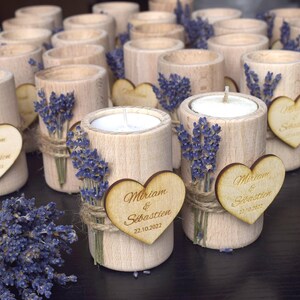 May include: A collection of small wooden candle holders with a heart-shaped tag that says "Miriam & Sebastien 22.10.2022". Each holder is decorated with dried lavender and twine.