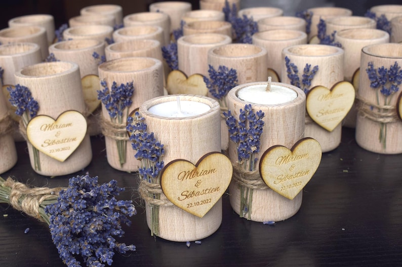 May include: A collection of small wooden candle holders with a heart-shaped tag that says "Miriam & Sebastien 22.10.2022". Each holder is decorated with dried lavender and twine.