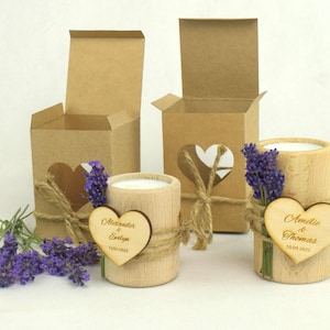 May include: Two wooden candle holders with personalized heart-shaped wooden tags. The tags are engraved with the names "Alexander & Evelyn" and "Amelie & Thomas" along with their wedding dates. The candle holders are decorated with lavender sprigs and twine.