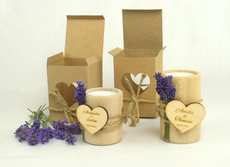 May include: Two wooden candle holders with personalized heart-shaped wooden tags. The tags are engraved with the names "Alexander & Evelyn" and "Amelie & Thomas" along with their wedding dates. The candle holders are decorated with lavender sprigs and twine.