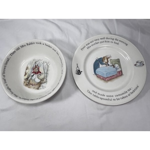 May include: A white ceramic bowl and plate set featuring illustrations of Peter Rabbit. The bowl shows a rabbit with a basket, and the plate depicts a rabbit in bed with text reading: Peter was not very well during the evening. His mother put him to bed.