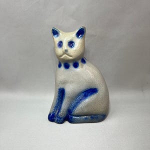 May include: A white ceramic mug with a black handle and the text "But First, Coffee" in a black, handwritten-style font. The mug is on a white surface.