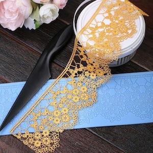 Può includere: Bordura in pizzo dorata per la decorazione di torte. Il pizzo è delicato e intricato, con un motivo floreale. È mostrato su uno stampo in silicone blu.