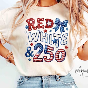Puede incluir: Una camiseta de manga corta color marfil con un estampado gráfico que incluye el texto RED WHITE & 250 en colores rojo, blanco y azul. El diseño presenta un lazo azul y varias formas de estrellas, con la palabra Ivory en la esquina superior.
