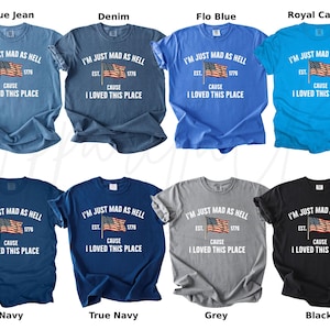 May include: A collection of eight t-shirts in various colors, including blue, navy, grey, and black. Each shirt features the text "I'M JUST MAD AS HELL" with an American flag graphic and the phrase "CAUSE I LOVED THIS PLACE."