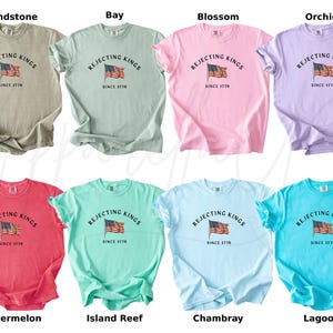 May include: A collection of eight short-sleeved t-shirts in various colors, including beige, green, pink, purple, red, teal, light blue, and turquoise. Each shirt features the text "Rejecting Kings Since 1776" with an American flag graphic.