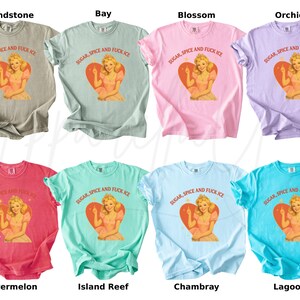 Peut inclure: Huit t-shirts de diff&eacute;rentes couleurs, dont beige, vert, rose, violet, rouge, sarcelle, bleu clair et turquoise. Chaque chemise pr&eacute;sente un graphisme d'une femme &agrave; l'int&eacute;rieur d'un c&oelig;ur avec le texte "SUGAR, SPICE AND FUCK ICE".