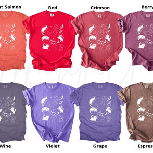 以下が含まれることがあります： 猫、惑星、星の白いグラフィックが特徴の、8色の異なる色のTシャツのコレクション。色は、明るいサーモン、赤、クリムゾン、ベリー、ワイン、バイオレット、グレープ、エスプレッソが含まれます。シャツは半袖です。
