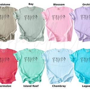 May include: Ten different coloured t-shirts with a simple floral design and the colour name printed below each shirt. The colours are Sandstone, Bay, Blossom, Orchid, Watermelon, Island Reef, Chambray, Lagoon.