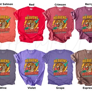 May include: A collection of eight t-shirts in various colors, including bright salmon, red, crimson, berry, wine, violet, grape, and espresso. Each shirt features a graphic of a roaring tiger with the text "HEAVENS are ROARING".