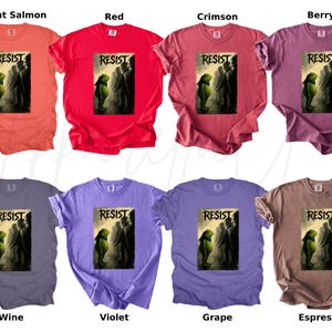 Pu&ograve; includere: Una collezione di otto t-shirt in vari colori, tra cui salmone brillante, rosso, cremisi, bacca, vino, viola, uva e espresso. Ogni maglietta presenta la parola "RESIST" sopra una grafica di figure.