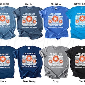 May include: A collection of t-shirts in various colors, including blue, navy, gray, and black. Each shirt features the text "ABOLISH ICE" above a floral design with orange flowers and the text "NO HUMAN IS ILLEGAL" below.