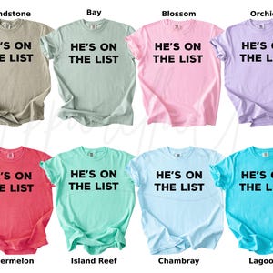 May include: Eight t-shirts in a range of colours, such as beige, pale green, pink, and lilac. Each shirt features the text "HE'S ON THE LIST" in bold black lettering. The shirts are labelled with colour names.