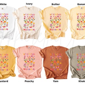 Pode incluir: Uma cole&ccedil;&atilde;o de camisetas em v&aacute;rias cores, incluindo branco, marfim, manteiga, banana, mostarda, p&ecirc;ssego, inhame e c&aacute;qui. Cada camiseta apresenta um design floral com a frase "let kindness bloom" em cores.