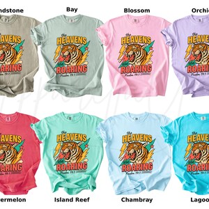 May include: A collection of eight t-shirts in various colors, each featuring a tiger graphic with the text "The Heavens are Roaring" and "Psalm 19:1". Colors include beige, light green, pink, purple, red, teal, light blue, and turquoise.