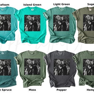 May include: A collection of eight different colored t-shirts. Each shirt features a black and white image of a group of people. The shirt colors include seafoam, island green, light green, sage, blue spruce, moss, pepper, and hemp.