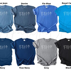 May include: A set of ten t-shirts in various colours, each featuring a white floral design. The colours include blue jean, denim, flo blue, royal caribe, navy, true navy, grey, and black.