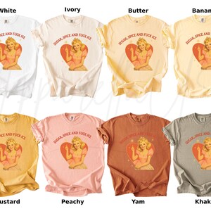 Peut inclure: Plusieurs t-shirts de couleurs vari&eacute;es, dont blanc, ivoire, beurre, banane, moutarde, p&ecirc;che, igname et kaki. Chaque t-shirt pr&eacute;sente un motif d'une femme dans un c&oelig;ur avec le texte "SUGAR, SPICE AND FUCK ICE".