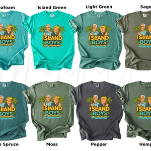 Pu&ograve; includere: Una collezione di otto t-shirt in vari colori, tra cui seafoam, verde isola, verde chiaro, salvia, abete blu, muschio, pepe e canapa. Ogni maglietta presenta una grafica di due uomini e il testo "ISLAND BOYS" con palme.