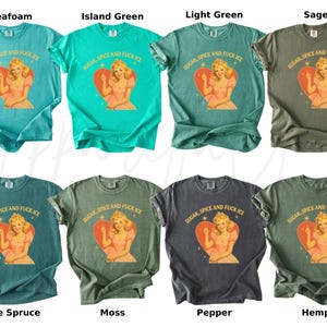 Peut inclure: Huit t-shirts de couleurs vari&eacute;es, dont vert d'eau, vert &icirc;le et sauge. Chaque t-shirt pr&eacute;sente un motif d'une femme dans un c&oelig;ur avec le texte "SUGAR, SPICE AND FUCK ICE".