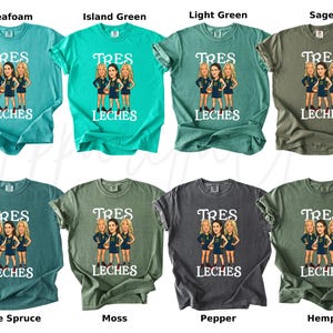 May include: A collection of eight t-shirts in various colors, including seafoam, island green, and sage. Each shirt features a graphic of three women and the text "TRES LECHES" in white. The shirts are short-sleeved.