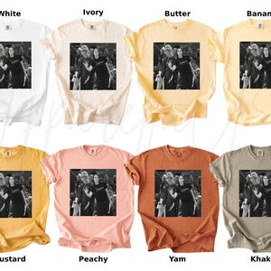 May include: A collection of eight t-shirts in various colors, including white, ivory, butter, banana, mustard, peachy, yam, and khaki. Each shirt features a black and white image of a group of people. The shirts are short-sleeved.