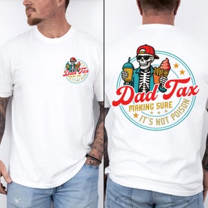 May include: White t-shirt featuring a graphic on the front and back. The front graphic is a circular design with the text "Dad Tax" and a skeleton holding a drink and ice cream. The back graphic is a larger version of the same design.
