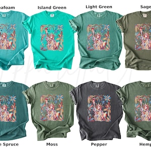 Puede incluir: Ocho camisetas en varios colores, incluyendo espuma de mar, verde isla, verde claro y salvia. Cada camiseta presenta un gr&aacute;fico de la Estatua de la Libertad rodeada de elementos florales. Los colores incluyen abeto azul, musgo, pimienta y c&aacute;&ntilde;amo.
