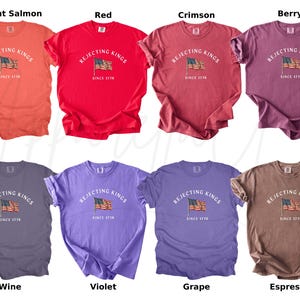 May include: A collection of eight t-shirts in various colors, including bright salmon, red, crimson, berry, wine, violet, grape, and espresso. Each shirt features the text "REJECTING KINGS SINCE 1776" with an American flag graphic.