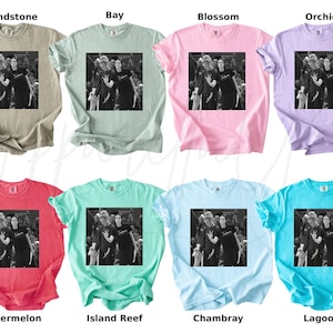 May include: A collection of eight t-shirts in various colors, including Sandstone, Bay, Blossom, Orchid, Watermelon, Island Reef, Chambray, and Lagoon. Each shirt features a black and white image of a group of people. The shirts are short-sleeved.