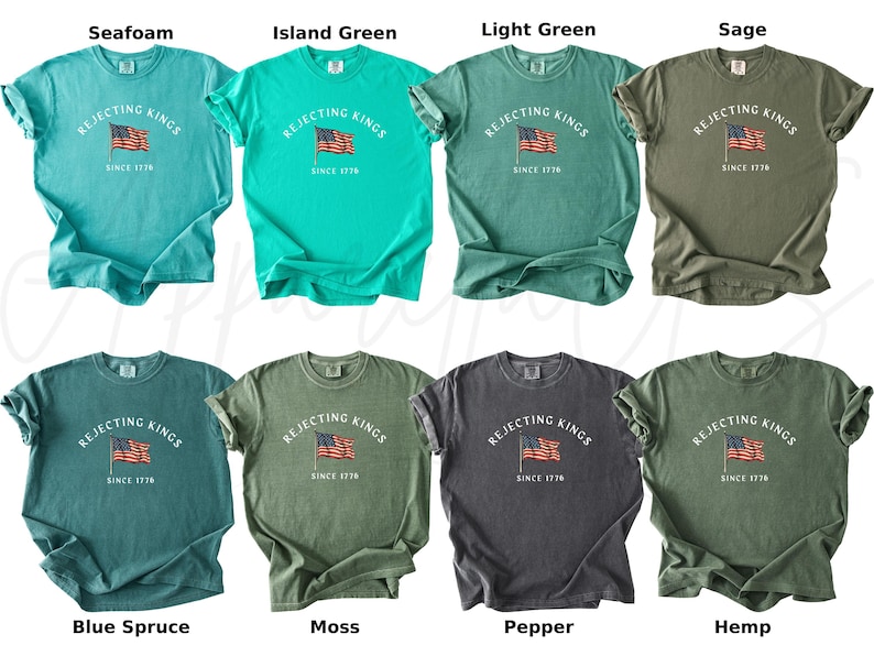 May include: A collection of t-shirts in various colors, including seafoam, island green, and sage. Each shirt features the text "REJECTING KINGS SINCE 1776" above an American flag graphic. The shirts are short-sleeved and have a casual style.