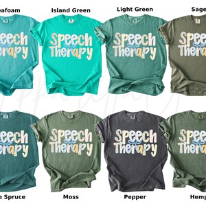 May include: A collection of eight t-shirts in various colors, including seafoam, island green, and sage. Each shirt displays the words "Speech Therapy" in a playful font with a floral design. The shirts are short-sleeved.