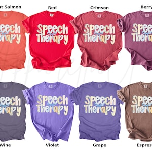 May include: A collection of eight t-shirts in various colors, including bright salmon, red, crimson, berry, wine, violet, grape, and espresso. Each shirt features the words "Speech Therapy" in a decorative font.
