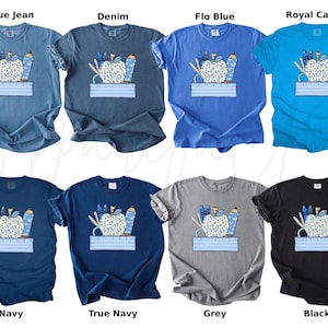 May include: A set of ten t-shirts featuring a graphic of a blue apple with school supplies, including pencils, crayons, scissors, and a ruler. The t-shirts are available in ten different colors: blue jean, denim, flo blue, royal caribe, navy, true navy, grey, black, white, and pink.