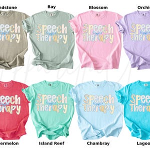 May include: A collection of eight t-shirts in various colors, including tan, green, pink, purple, red, teal, light blue, and turquoise. Each shirt displays the words "Speech Therapy" in a decorative font.