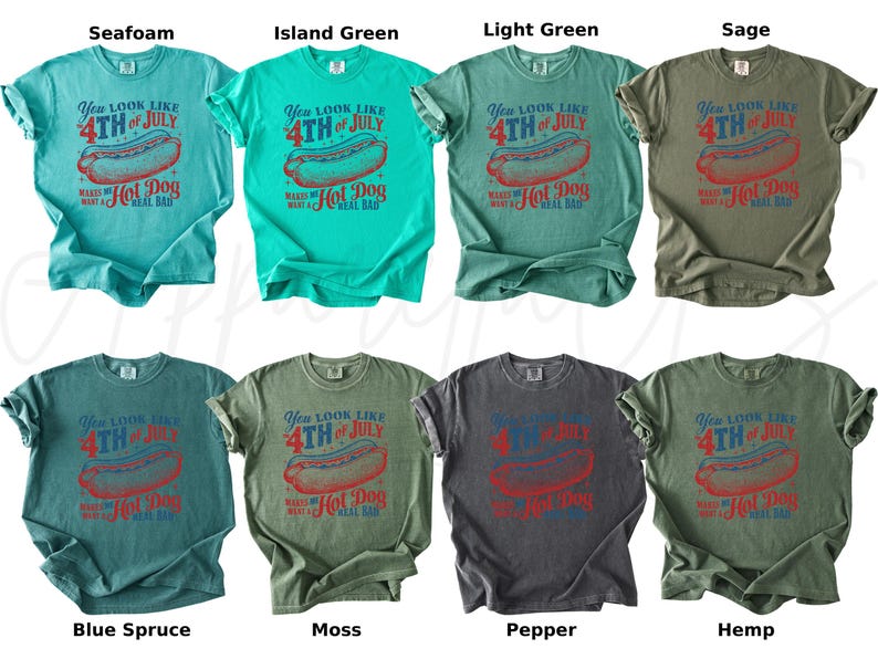May include: Collection of t-shirts in various colors, each featuring a graphic with a hot dog and the text "You look like 4th of July makes me want a hot dog real bad". Colors include seafoam, island green, light green, sage, blue spruce, moss, pepper, and hemp.