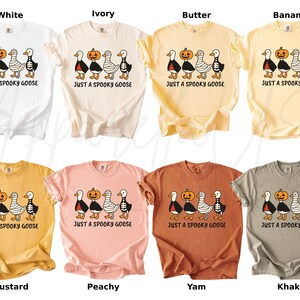 K&ouml;nnte beinhalten: Acht T-Shirts in verschiedenen Farben, darunter Wei&szlig;, Elfenbein und Senf. Jedes Shirt zeigt eine Grafik von vier G&auml;nsen, einem K&uuml;rbis und dem Text "JUST A SPOOKY GOOSE". Ideal f&uuml;r Halloween, diese T-Shirts sind in verschiedenen Gr&ouml;&szlig;en erh&auml;ltlich.