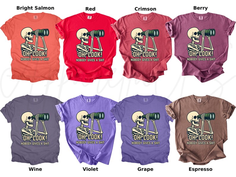 Op de afbeelding: Een verzameling van acht T-shirts in verschillende kleuren, elk met een skelet dat door een verrekijker kijkt. De tekst "OH LOOK! NOBODY GIVES A SHIT" staat onder het skelet. Kleuren zijn helder zalm, rood, karmozijn, bes, wijn, violet, druif en espresso.