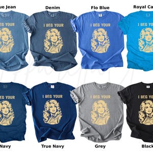 May include: A collection of eight short-sleeved crew neck t-shirts in various colors including blue, navy, grey, and black. Each shirt features a graphic print of a woman with blonde hair and the text I BEG YOUR printed in a light tan color.