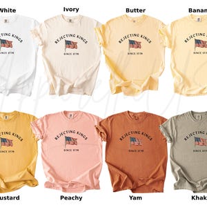 May include: A collection of eight t-shirts in various colors, including white, ivory, butter, banana, mustard, peachy, yam, and khaki. Each shirt features the text "REJECTING KINGS SINCE 1776" above an American flag graphic.
