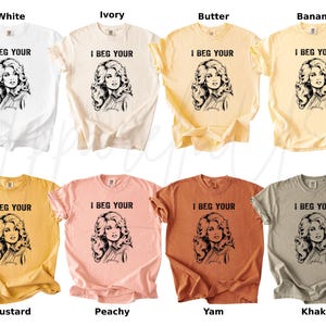 May include: Eight short-sleeved crew neck t-shirts in white, ivory, butter, banana, mustard, peachy, yam, and khaki colors. Each shirt features a black graphic print of a woman with voluminous hair and the text I BEG YOUR printed above the image.