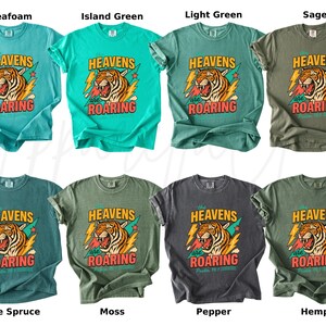 May include: A collection of eight t-shirts in various colors, including seafoam, island green, and sage. Each shirt features a graphic of a roaring tiger with the text "HEAVENS are ROARING".