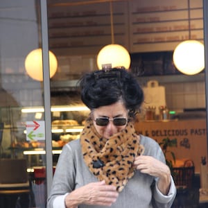 May include: A woman wearing a gray sweater and a brown and black animal print scarf. She is looking down and smiling.