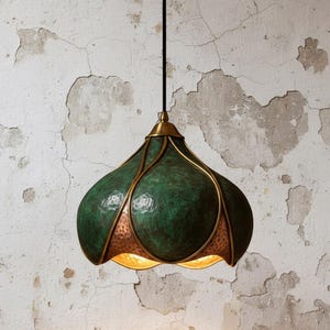 May include: A decorative pendant light with a green, textured shade and brass detailing. The shade has a distinctive, organic form with a copper-coloured interior. The light hangs from a black cord and features a brass-coloured top.