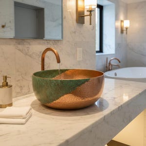 Puede incluir: Un lavabo decorativo de cobre y verde con un grifo a juego. El lavabo está sobre una encimera de mármol con un dispensador de jabón y toallas blancas dobladas. El baño tiene una bañera blanca y paredes de mármol.