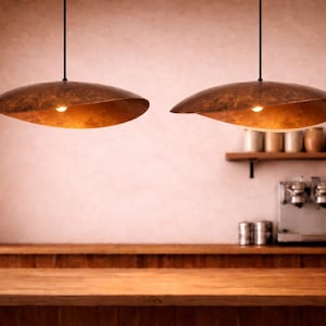Könnte beinhalten: Zwei Pendelleuchten mit einer einzigartigen, organischen Form hängen von der Decke. Die Lampenschirme sind in einem warmen, metallischen Braun gehalten und haben jeweils eine einzelne Glühbirne. Die Leuchten hängen über einer Holztheke.