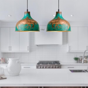 Puede incluir: Dos l&aacute;mparas colgantes con acabado turquesa y bronce cuelgan en una cocina. Las l&aacute;mparas tienen forma de c&uacute;pula con apariencia met&aacute;lica. La cocina cuenta con gabinetes, encimeras y una estufa blancos.