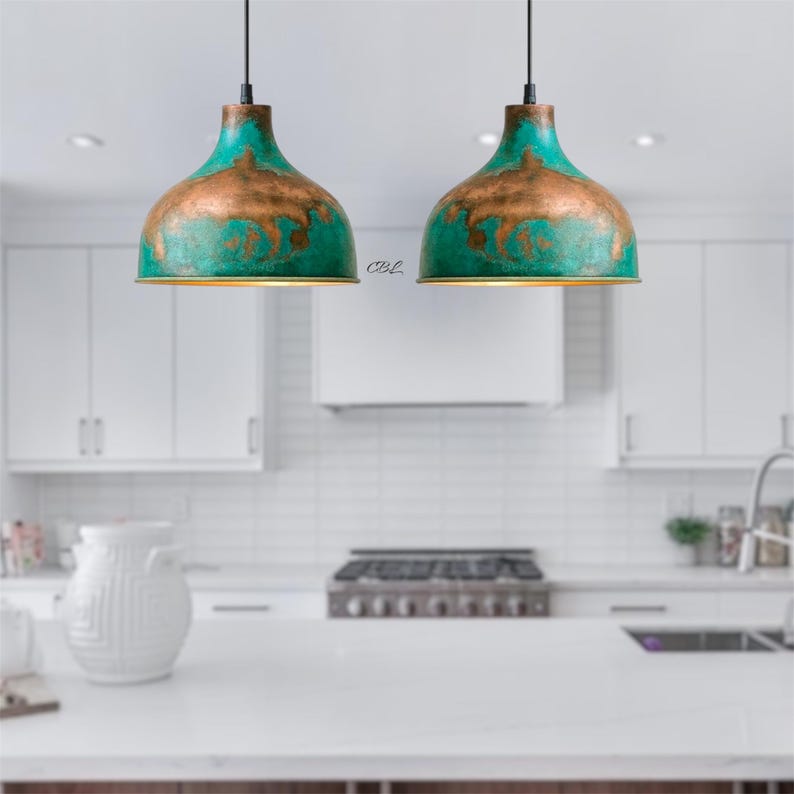 Puede incluir: Dos l&aacute;mparas colgantes con acabado turquesa y bronce cuelgan en una cocina. Las l&aacute;mparas tienen forma de c&uacute;pula con apariencia met&aacute;lica. La cocina cuenta con gabinetes, encimeras y una estufa blancos.
