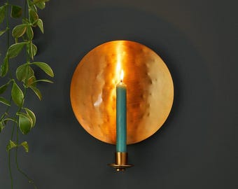 May include: A gold metal wall sconce with a hammered finish and a teal candle. The sconce is round and has a simple design.